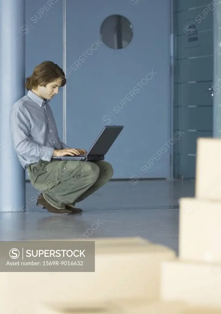 Businessman leaning against pole, using laptop, cardboard boxes in foreground