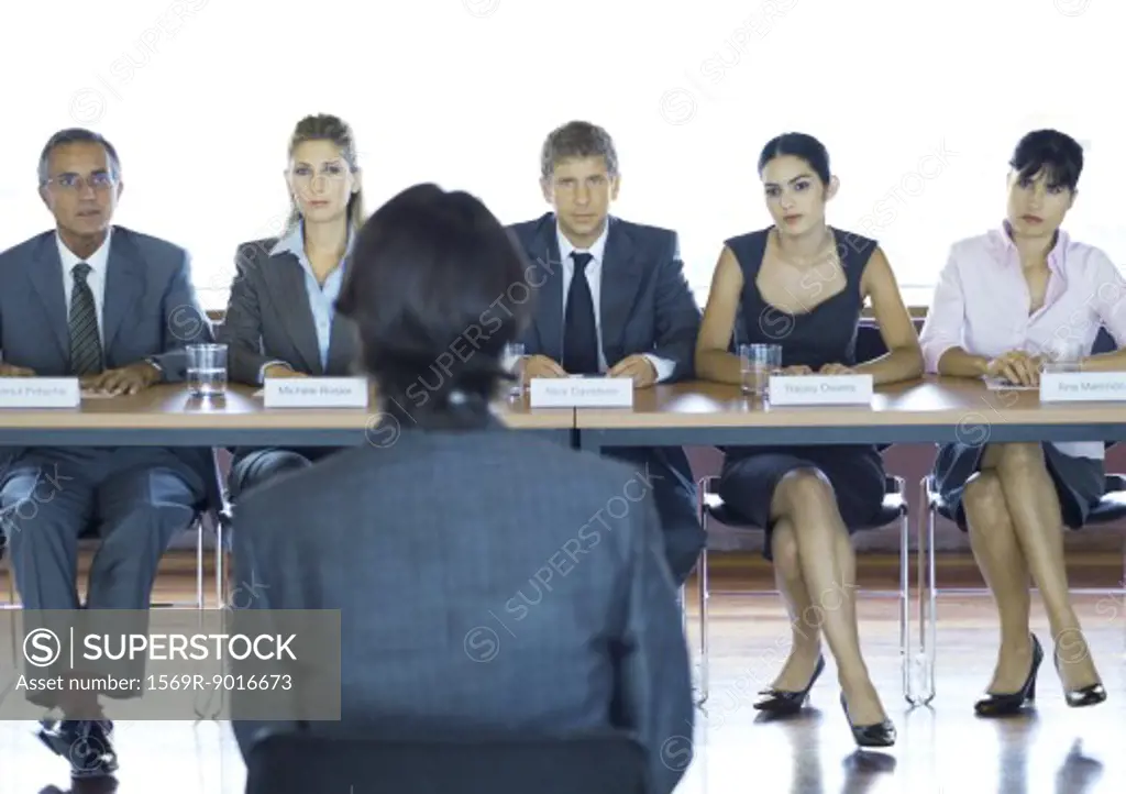 Executives sitting at conference table, looking at man in foreground