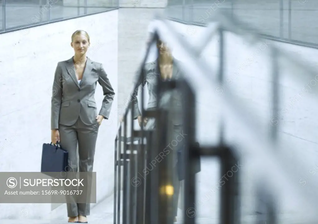Businesswoman standing holding briefcase, hand in pocket, portrait