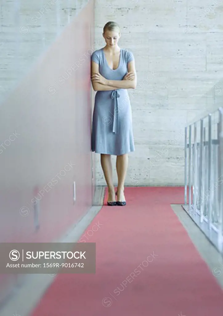 Woman standing, leaning against wall, head down, full length portrait