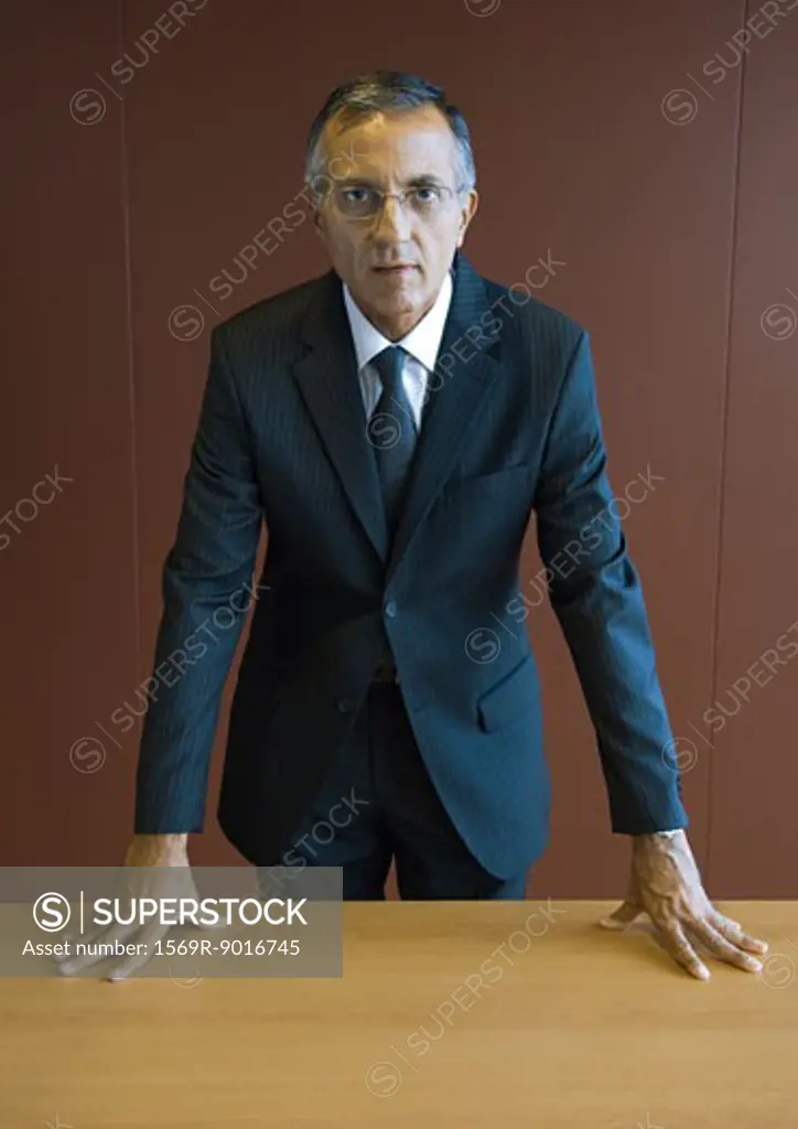 Businessman standing with hands on table, portrait
