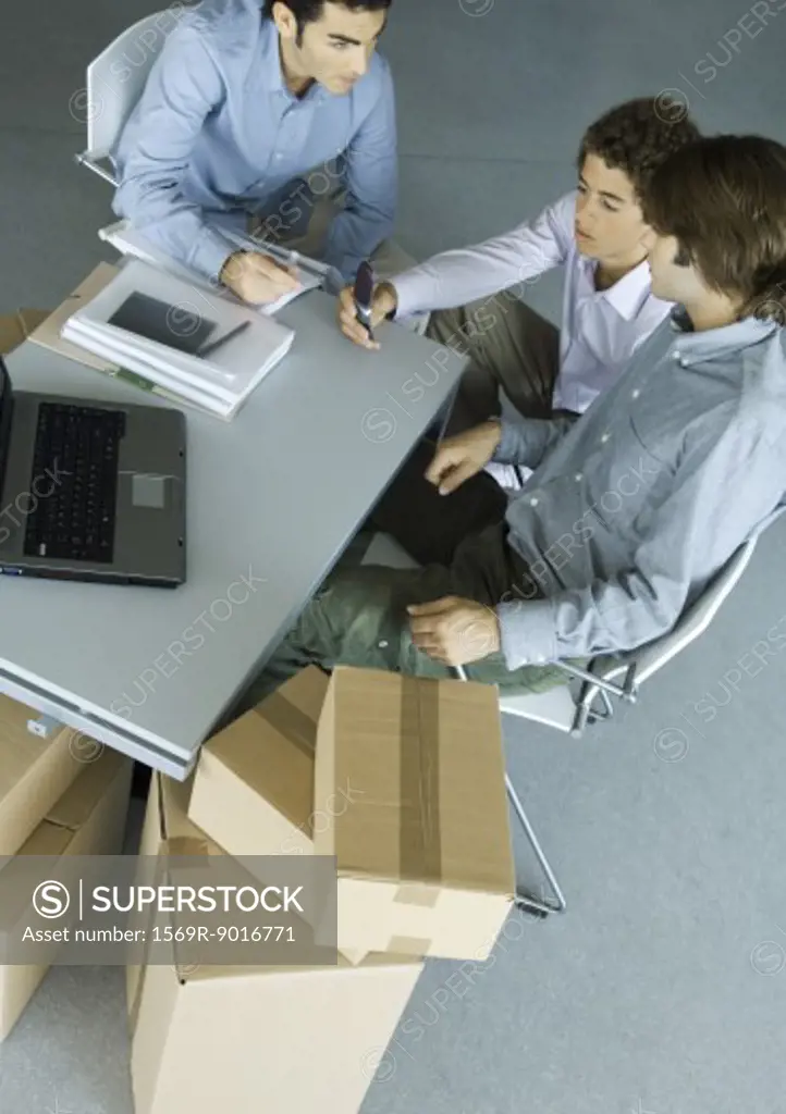 Three male colleagues grouped around desk, surrounded by cardboard boxes