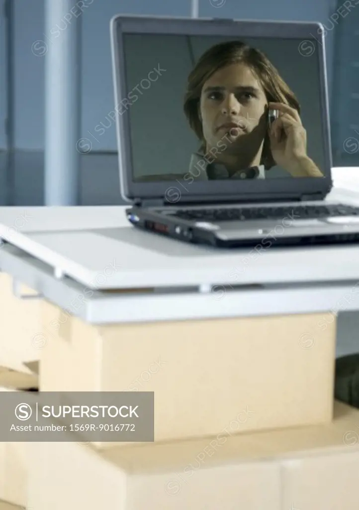 Image of man using cell phone reflected in laptop screen