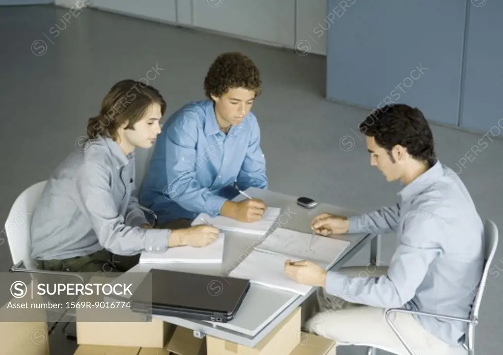 Three male colleagues sitting at table talking about documents