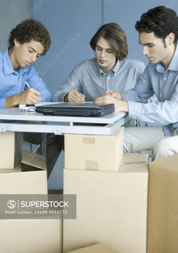 Three male colleagues working at table, cardboard boxes in foreground