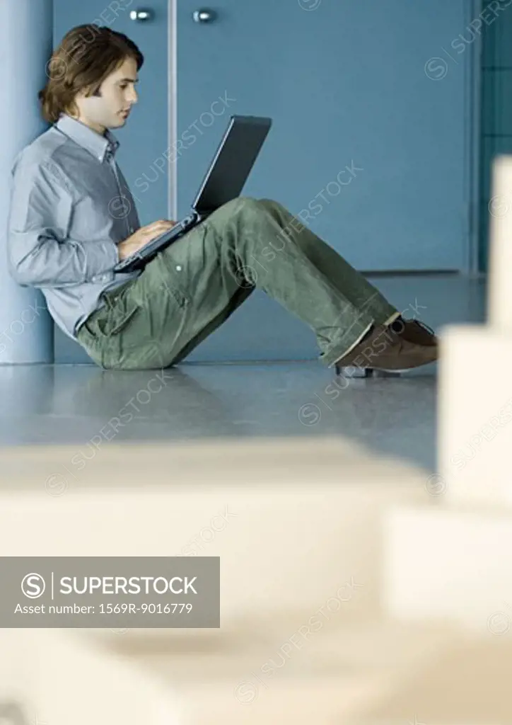 Young man sitting on floor using laptop, cardboard boxes in foreground