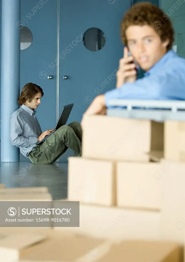 Young man sitting on floor using laptop, cardboard boxes in foreground