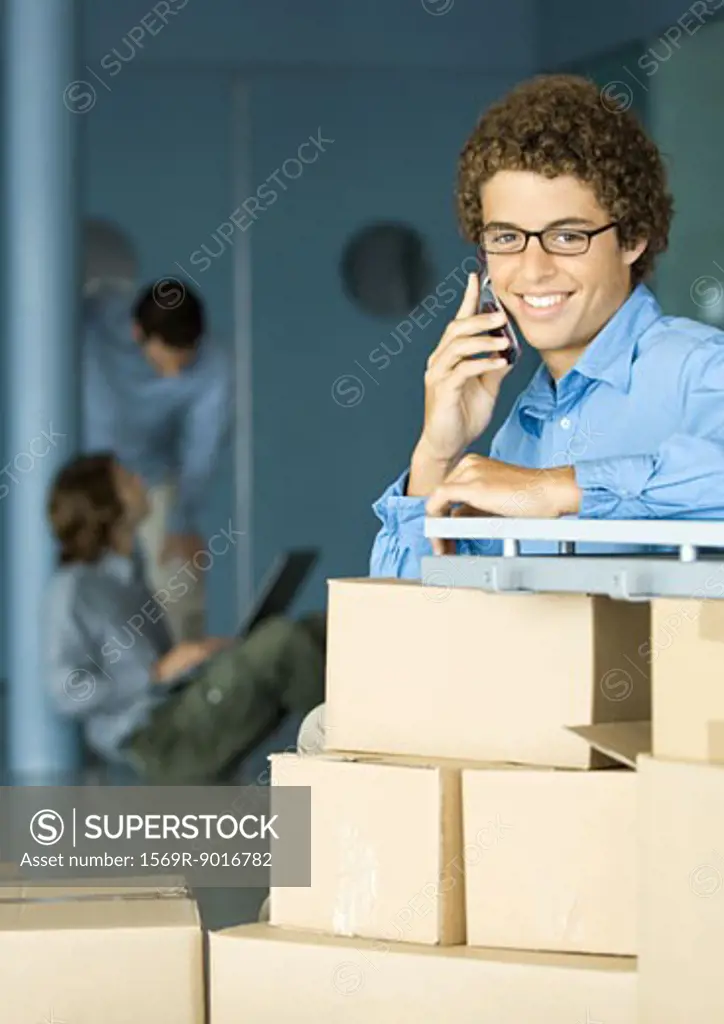 Young man using cell phone, cardboard boxes in foreground
