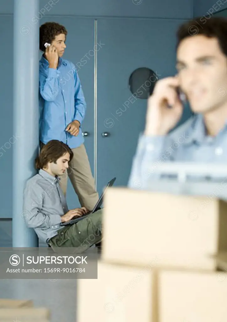 Male colleagues using laptop and cell phone, cardboard boxes in foreground