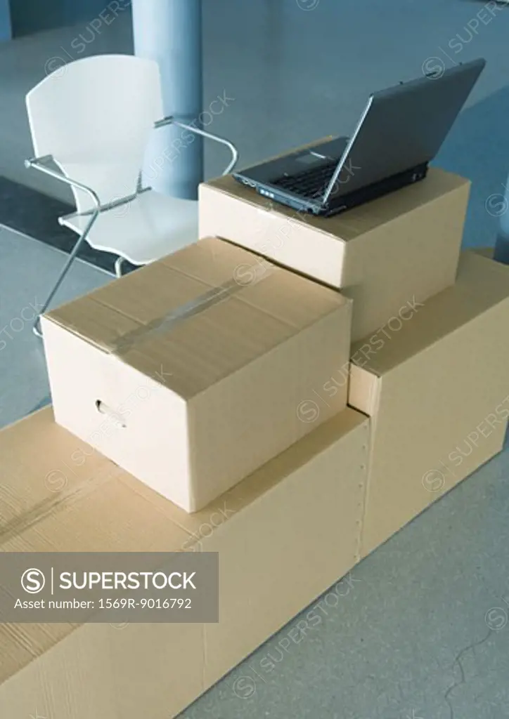 Open laptop on stack of cardboard boxes, and empty chair
