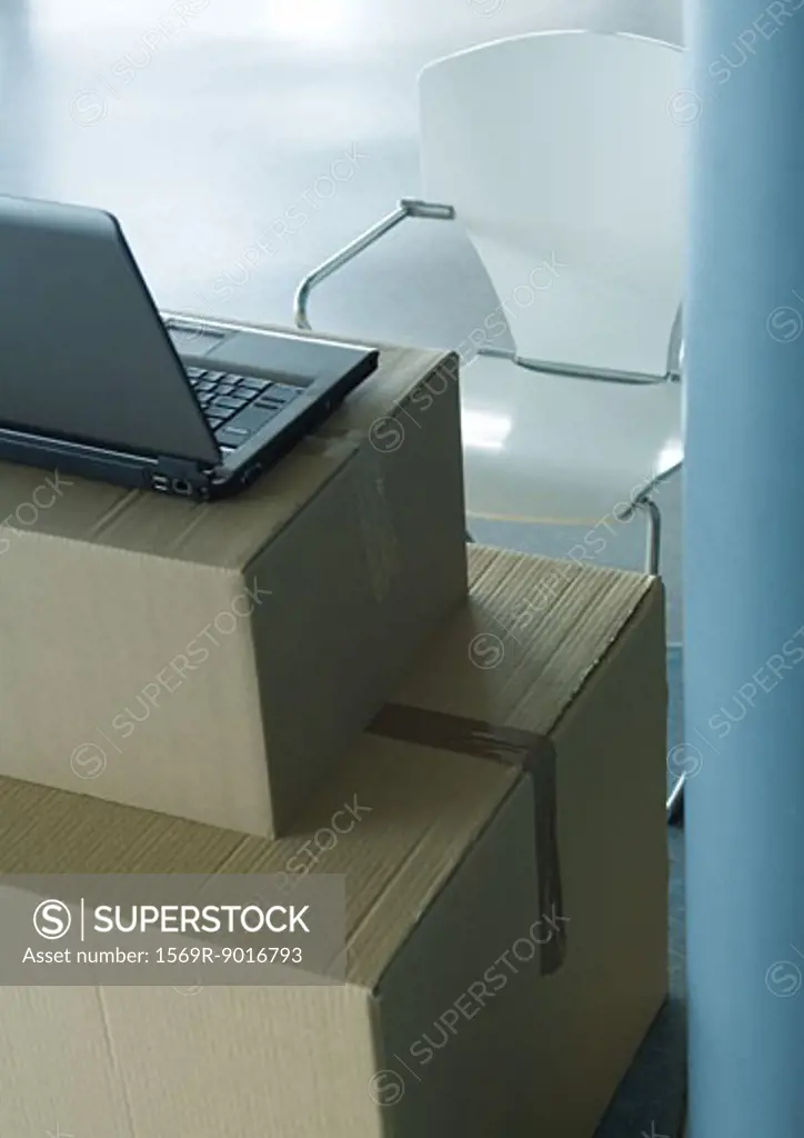 Open laptop on stack of cardboard boxes, and empty chair