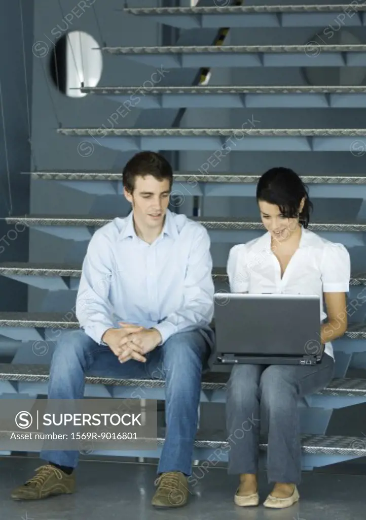 Two colleagues talking, sitting on stairs with laptop