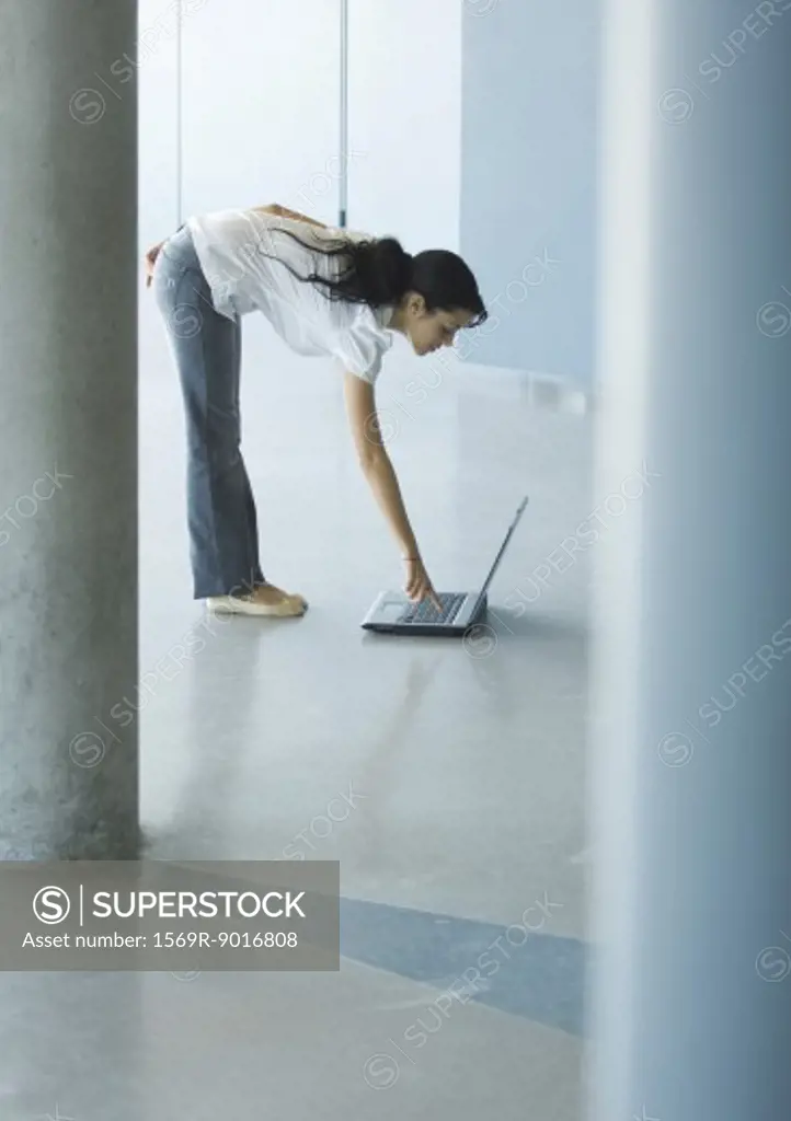 Young woman bending over, pressing key on laptop