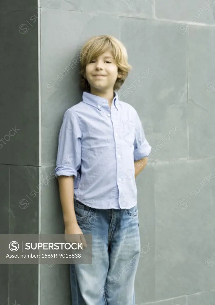Boy leaning against wall, smiling, portrait