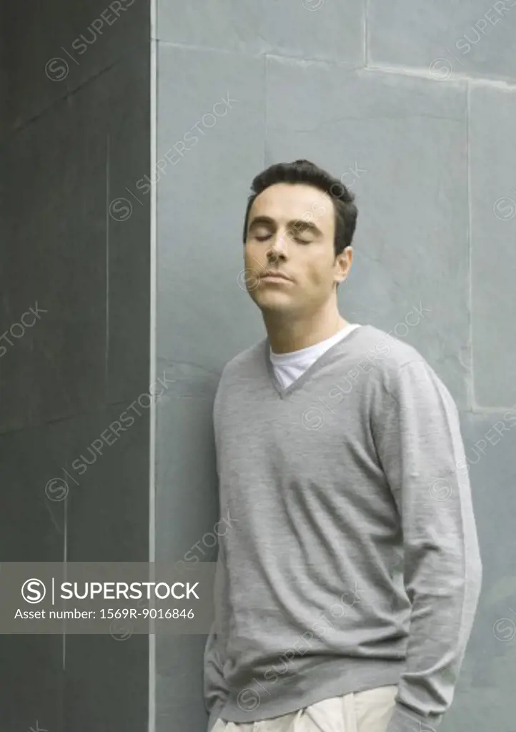 Man leaning against wall, closing eyes