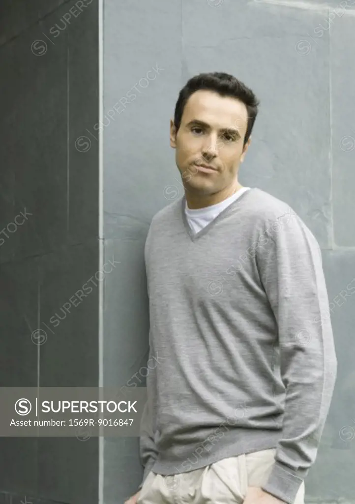Man leaning against wall, looking at camera, waist up, portrait