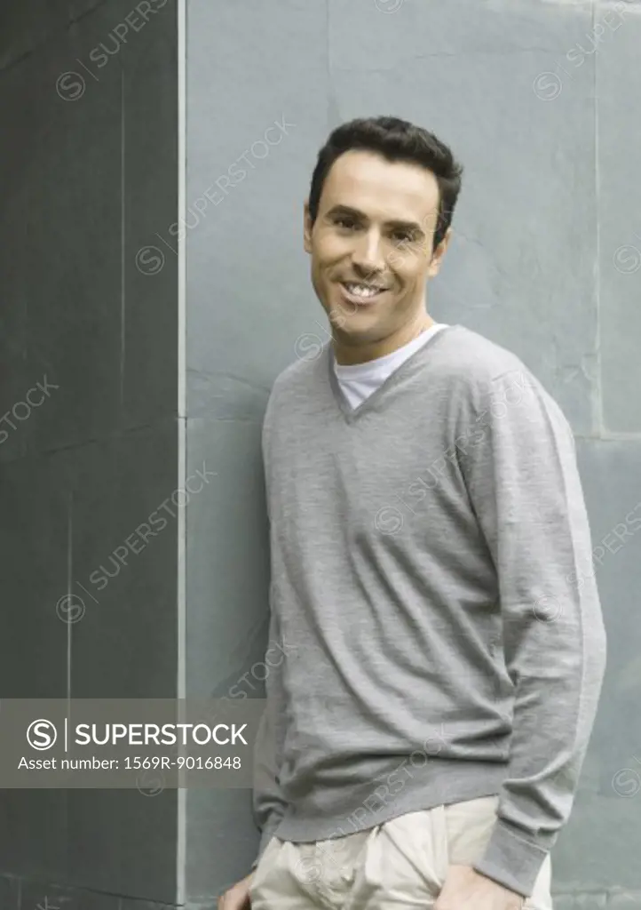 Man leaning against wall, smiling at camera, waist up, portrait