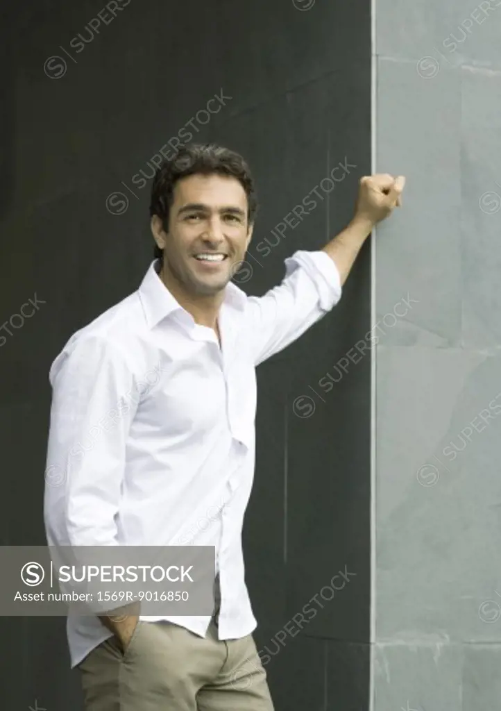 Man standing with hand on corner of wall, smiling at camera, portrait