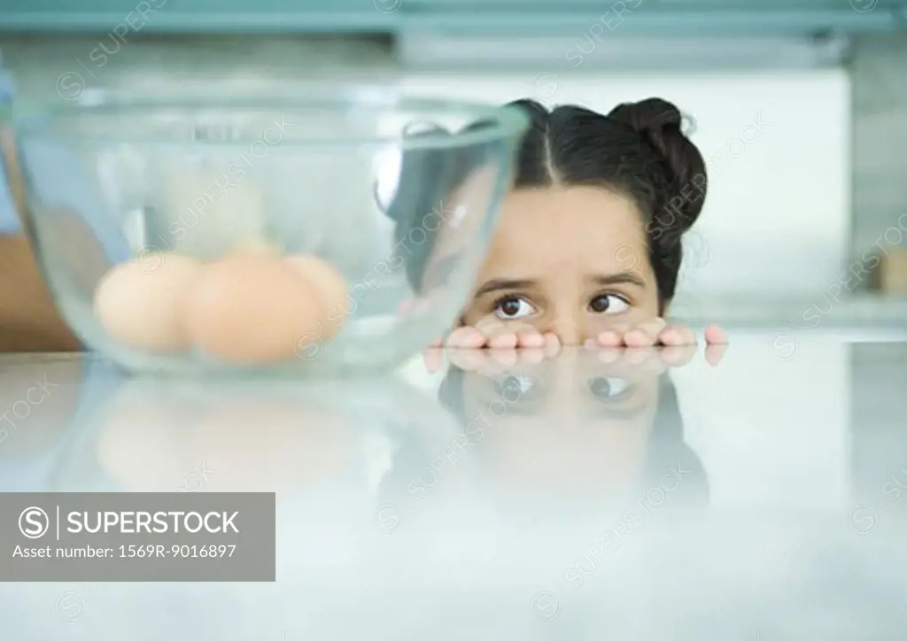 Girl looking over edge of counter at eggs in mixing bowl