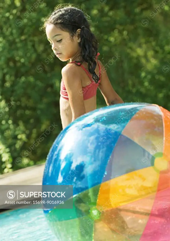 Girl standing in pool, with beach ball