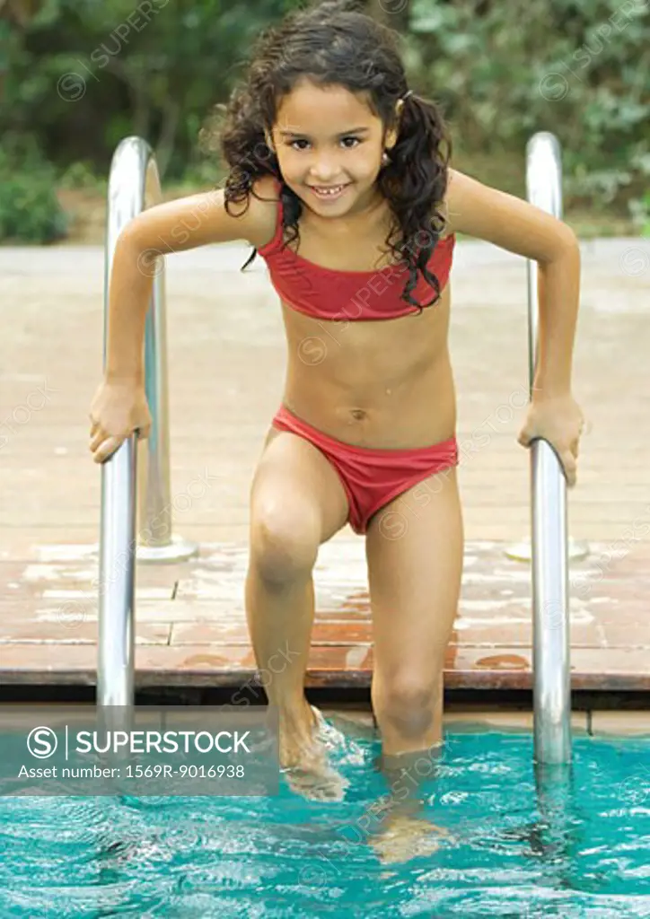 Girl standing on pool ladder, smiling at camera