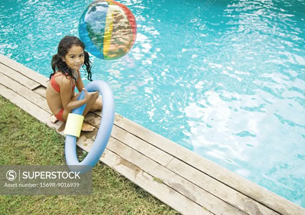 Girl sitting by edge of pool, holding floating ring