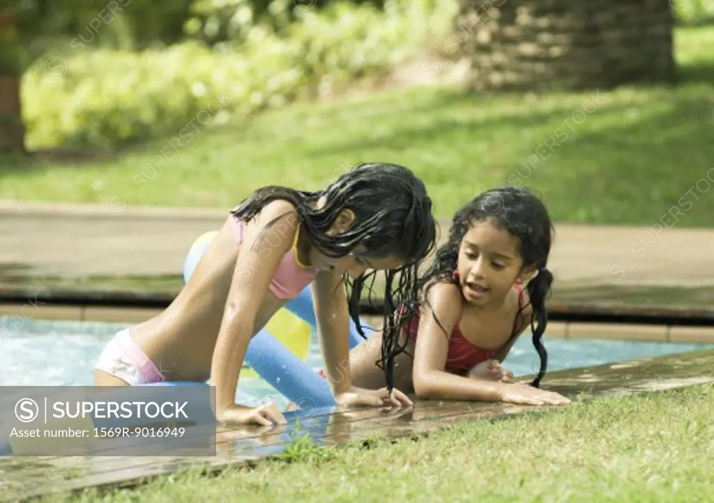 Two girls leaning on edge of pool, talking