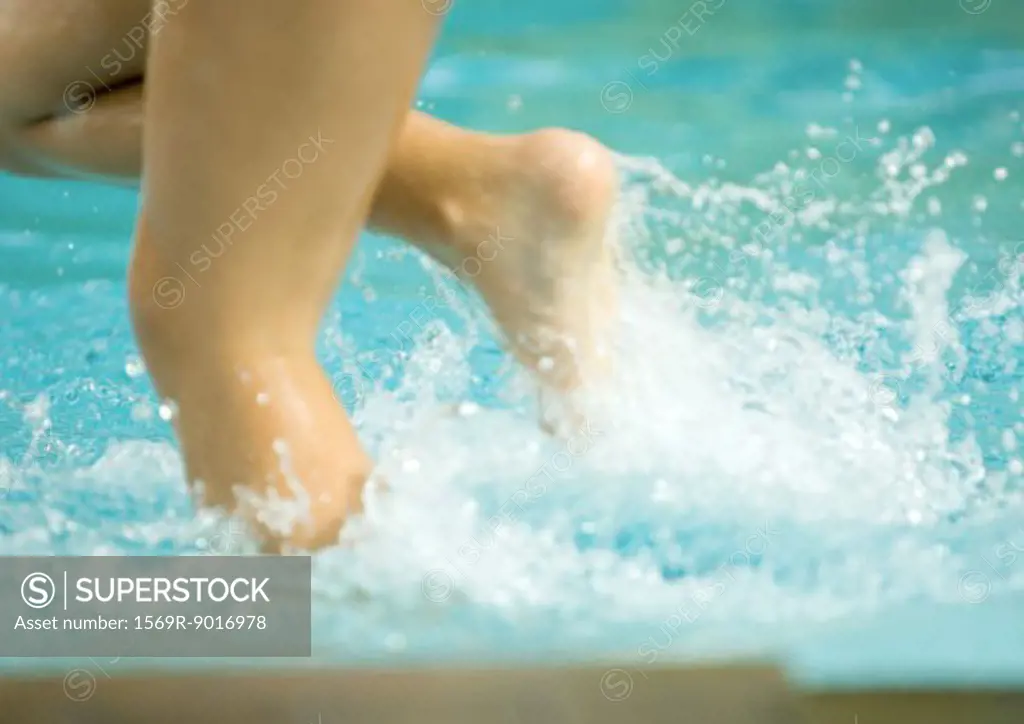 Child splashing in pool water, close-up of legs