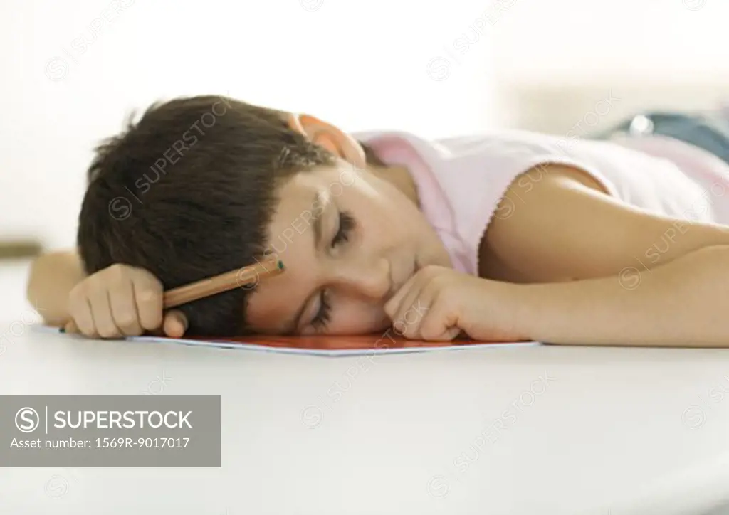 Child falling asleep with head on notebook and pencil in hand