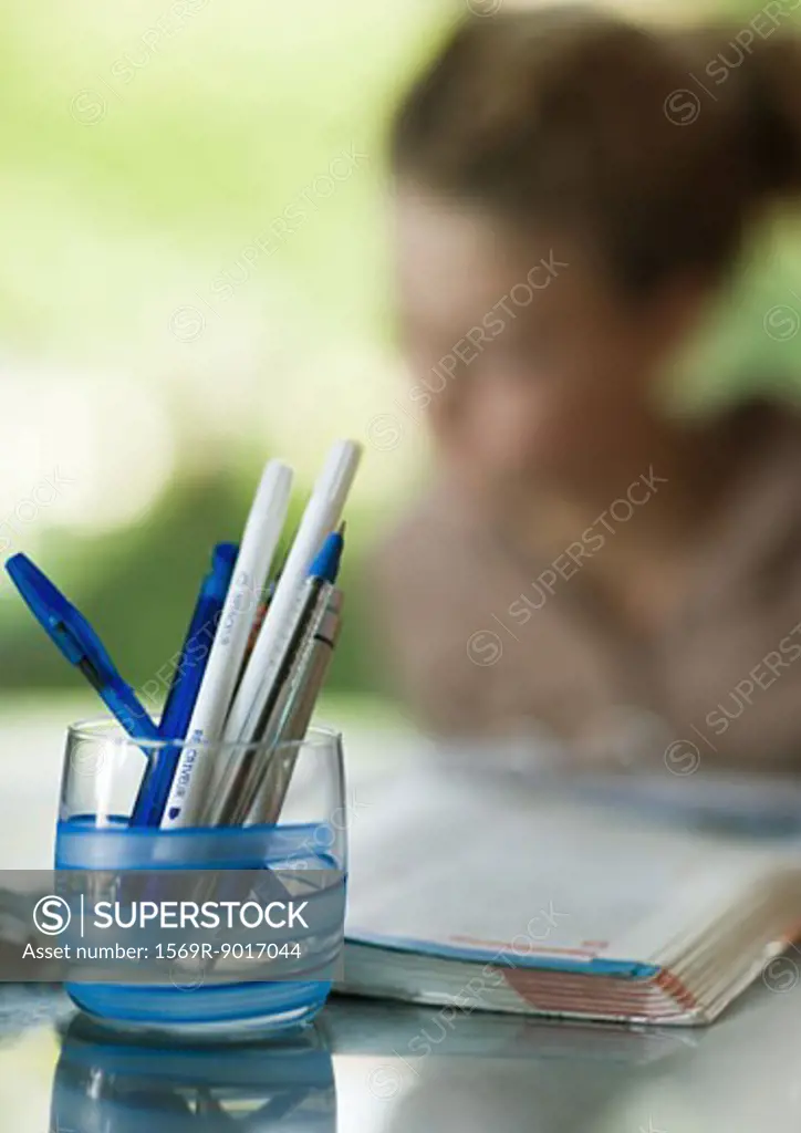 Glass full of pens, child doing homework in background