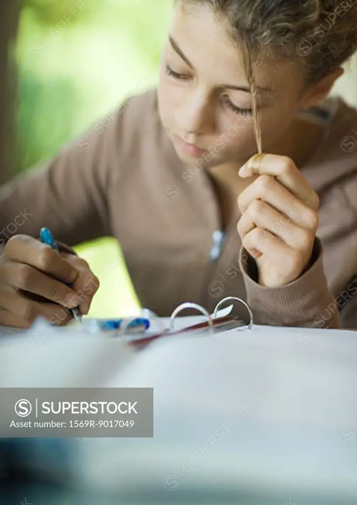 Preteen girl doing homework, twirling strand of hair