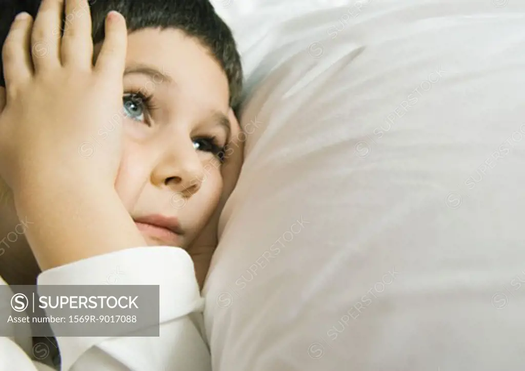 Child lying in bed holding head
