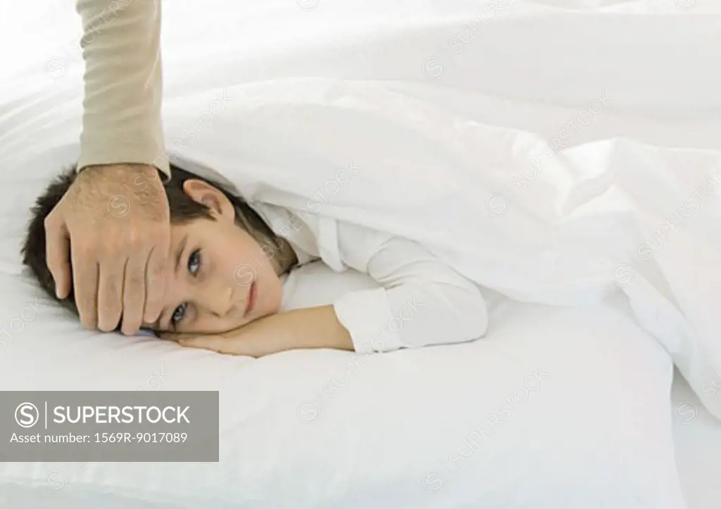 Child lying in bed with father's hand on forehead