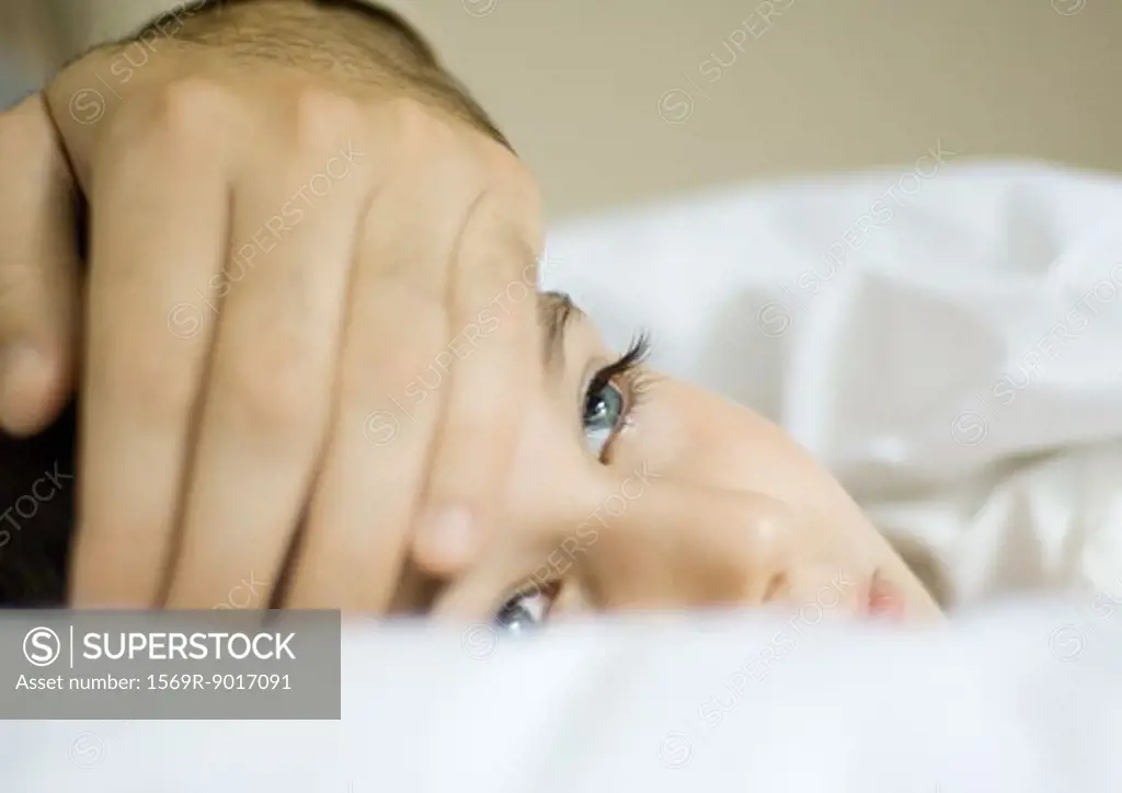 Child lying in bed with father's hand on forehead