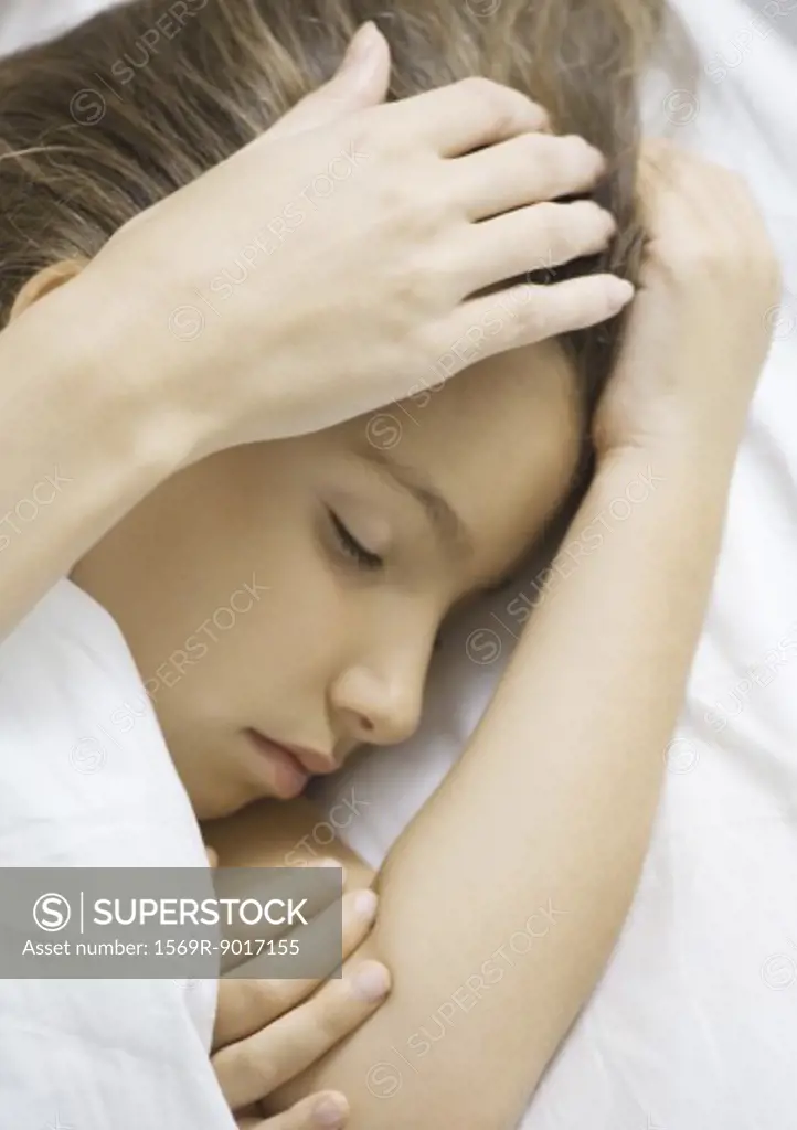 Girl sleeping in bed, mother's hand stroking head