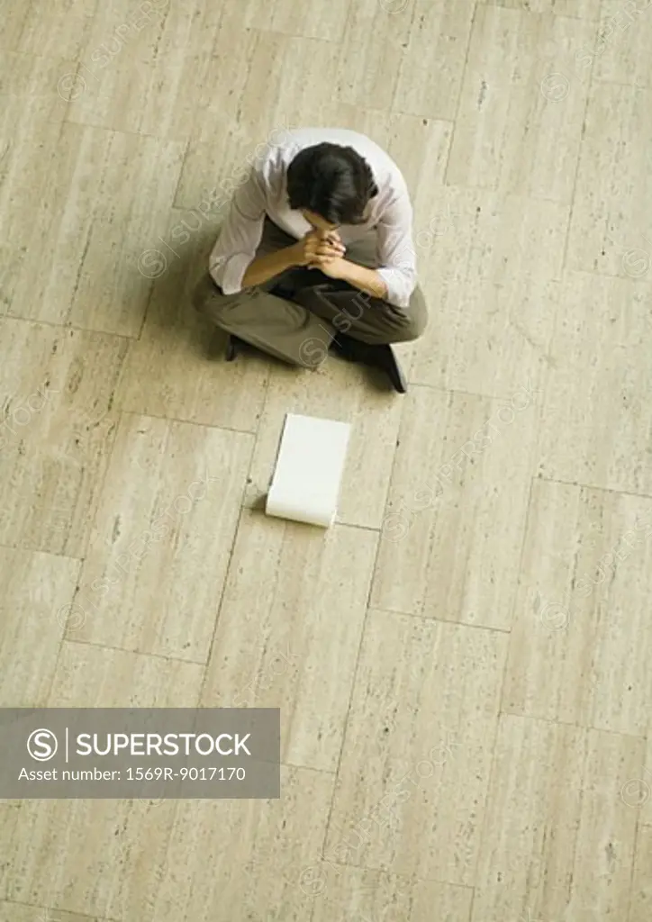 Man sitting on floor with blank pad of paper, high angle view