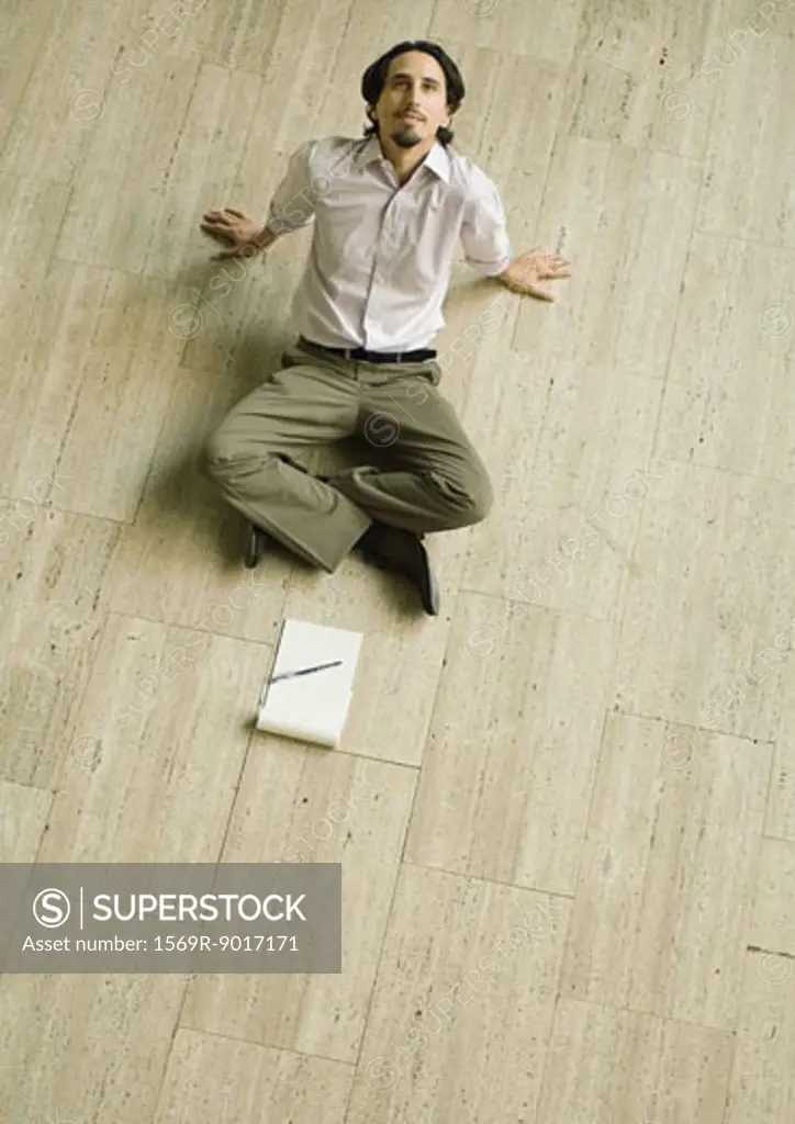 Man sitting on floor with pad of paper in front of him, leaning back, high angle view