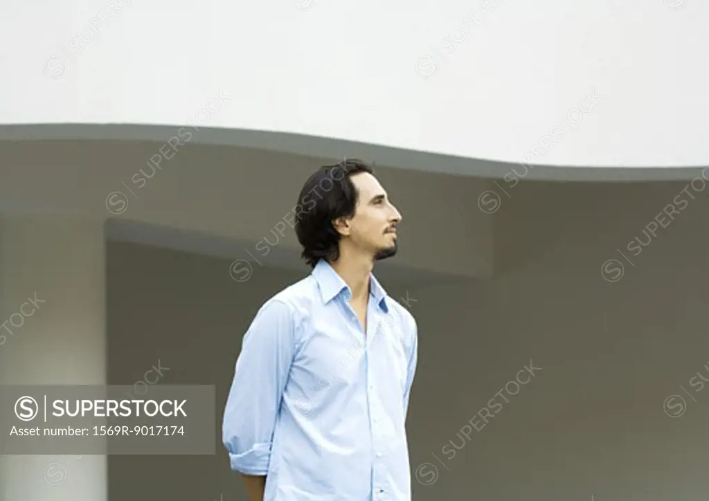 Man standing with arms behind back, looking out of frame