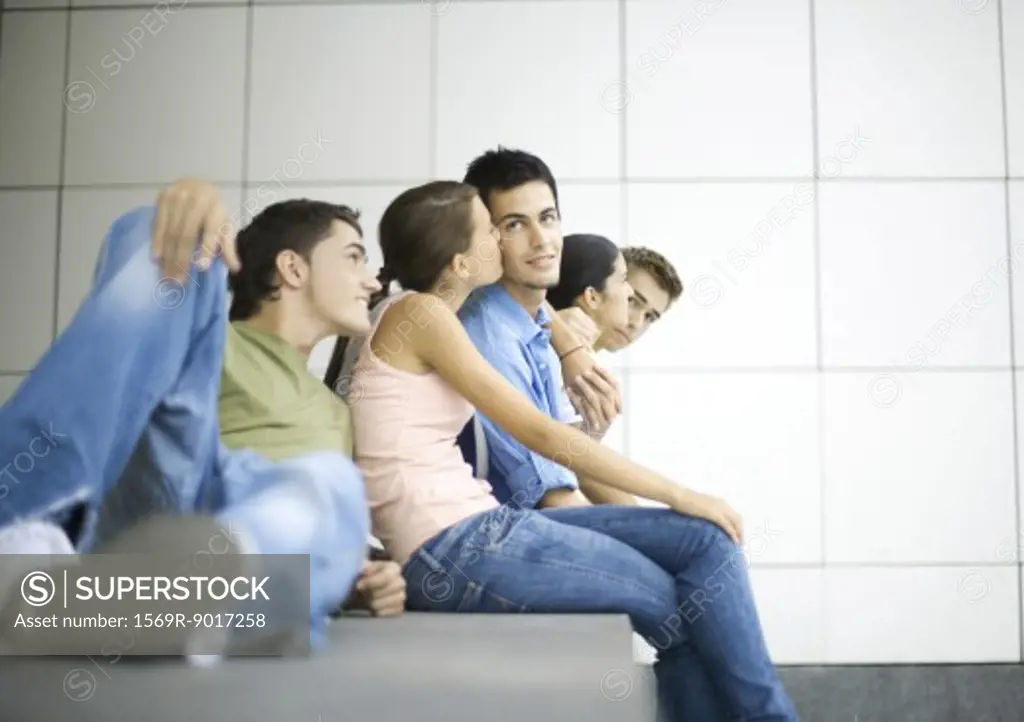 Group of teenage friends sitting together, girl kissing boy on cheek
