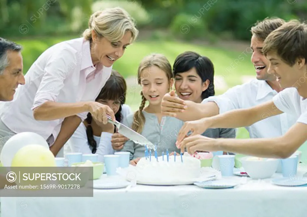 Outdoor birthday party, mature woman cutting birthday cake