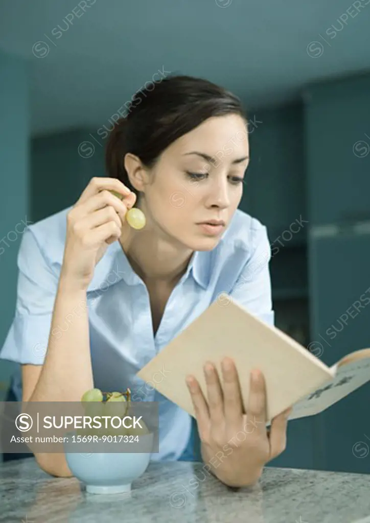 Woman reading book and eating grapes
