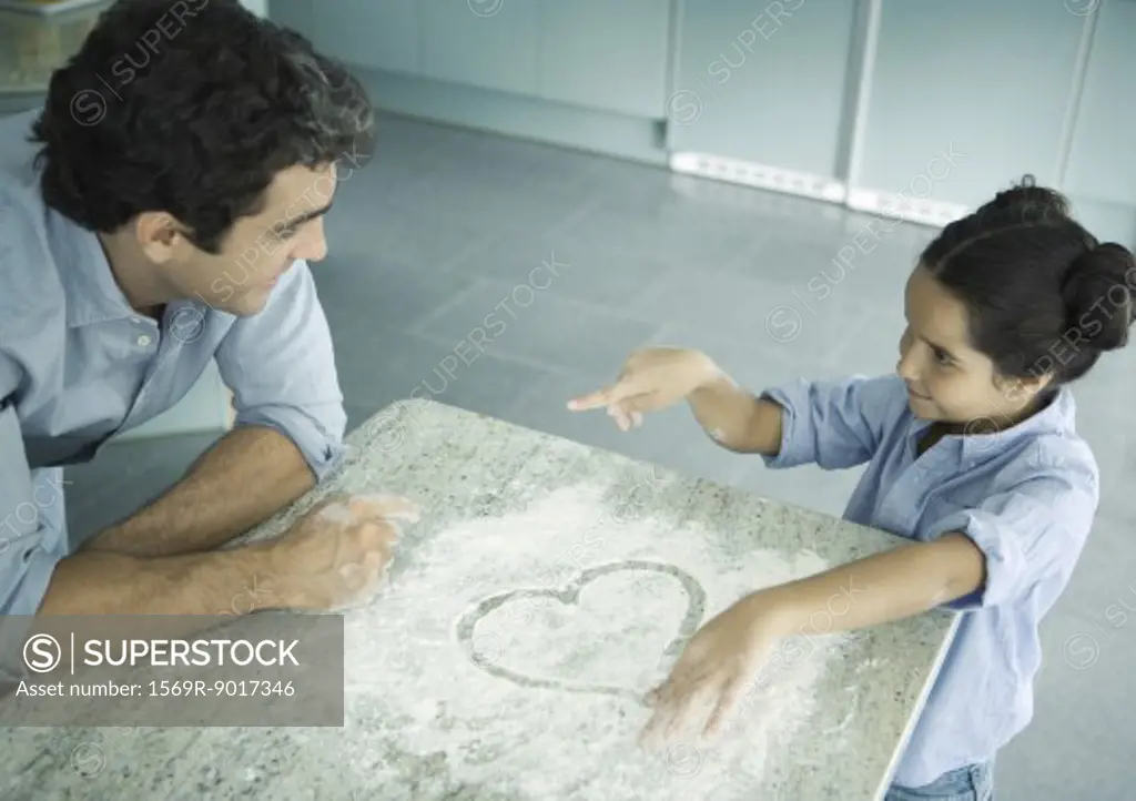 Father and daughter cooking together, heart drawn in flour on counter