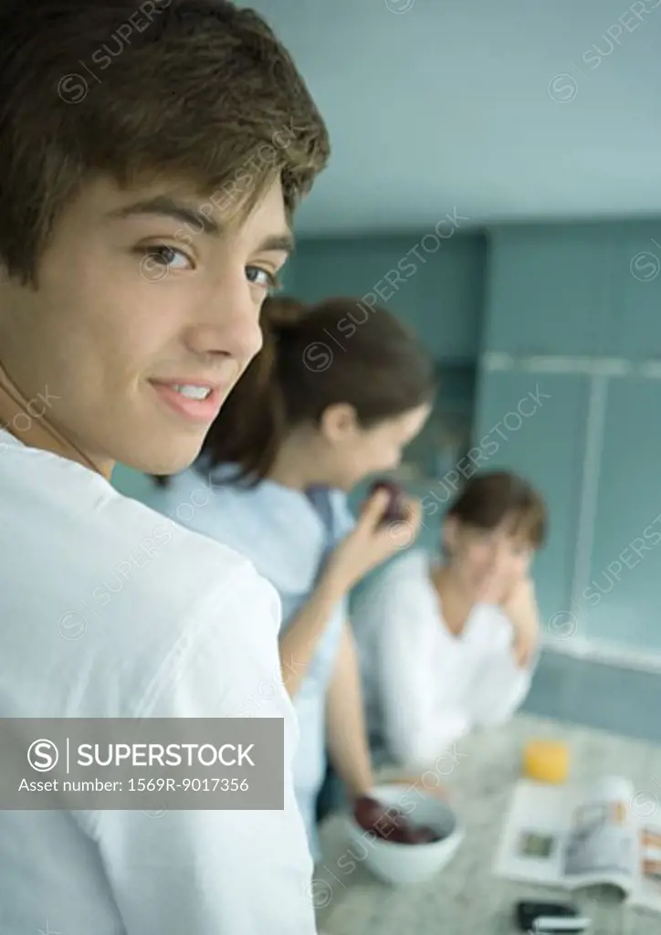 Teenage boy with family in kitchen, looking over shoulder
