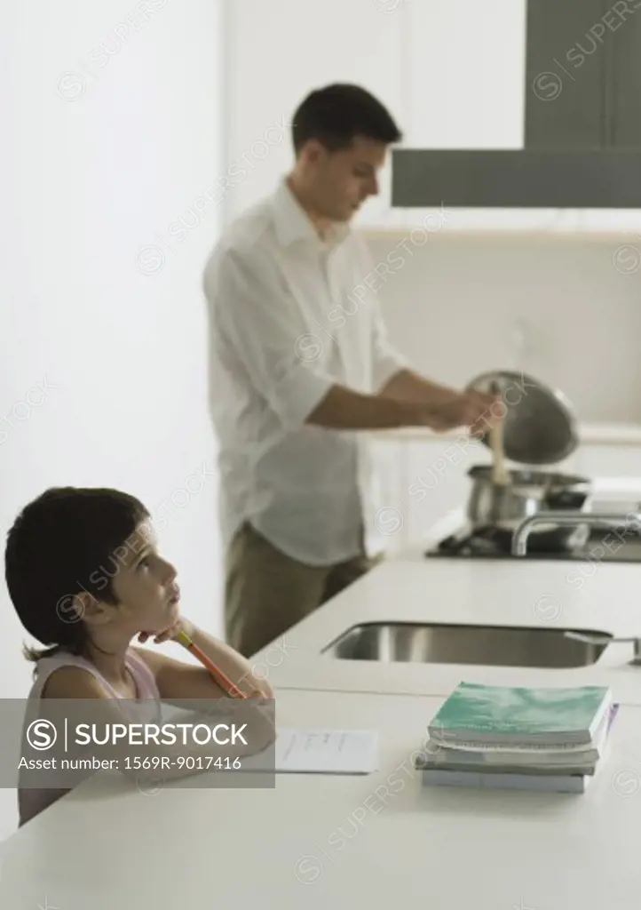 Child doing homework while father cooks meal