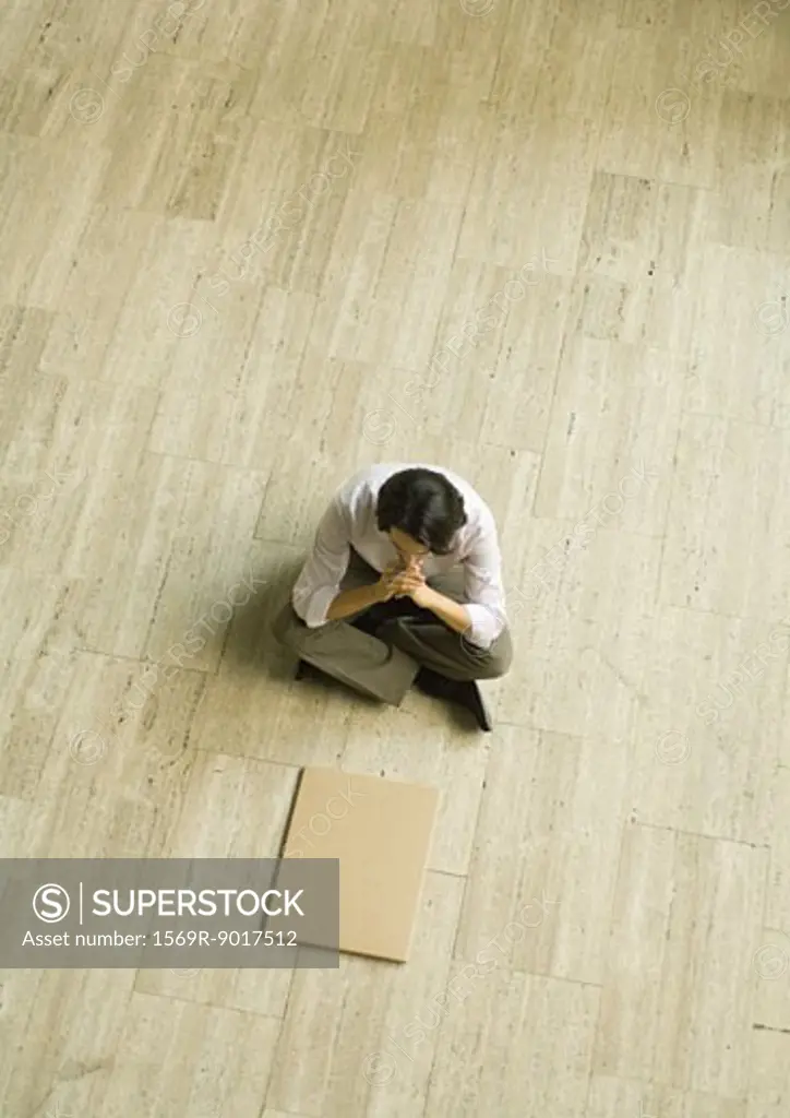 Man sitting on floor with pen, looking at blank kraft paper, high angle view
