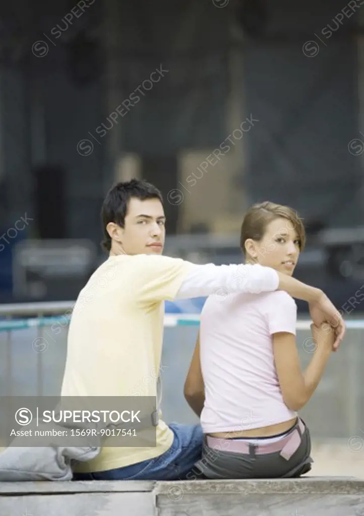 Teen couple sitting, looking over shoulder