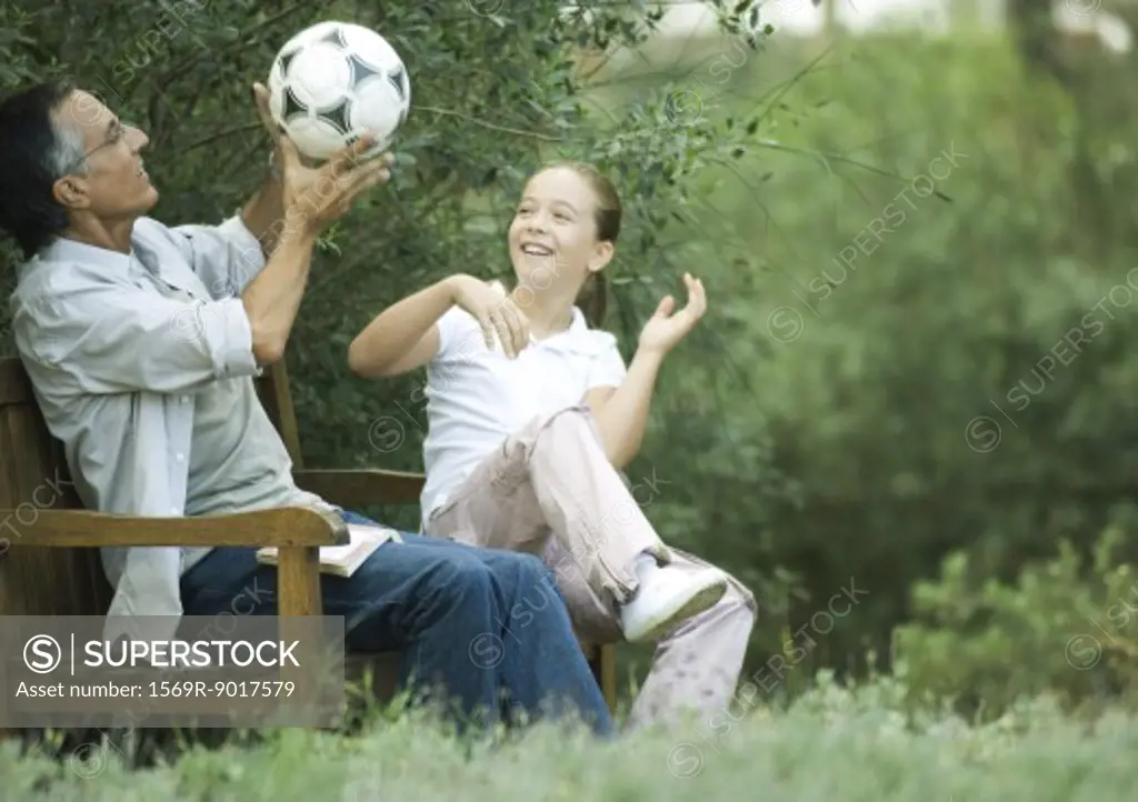 Girl and grandfather sitting together, playing with soccer ball