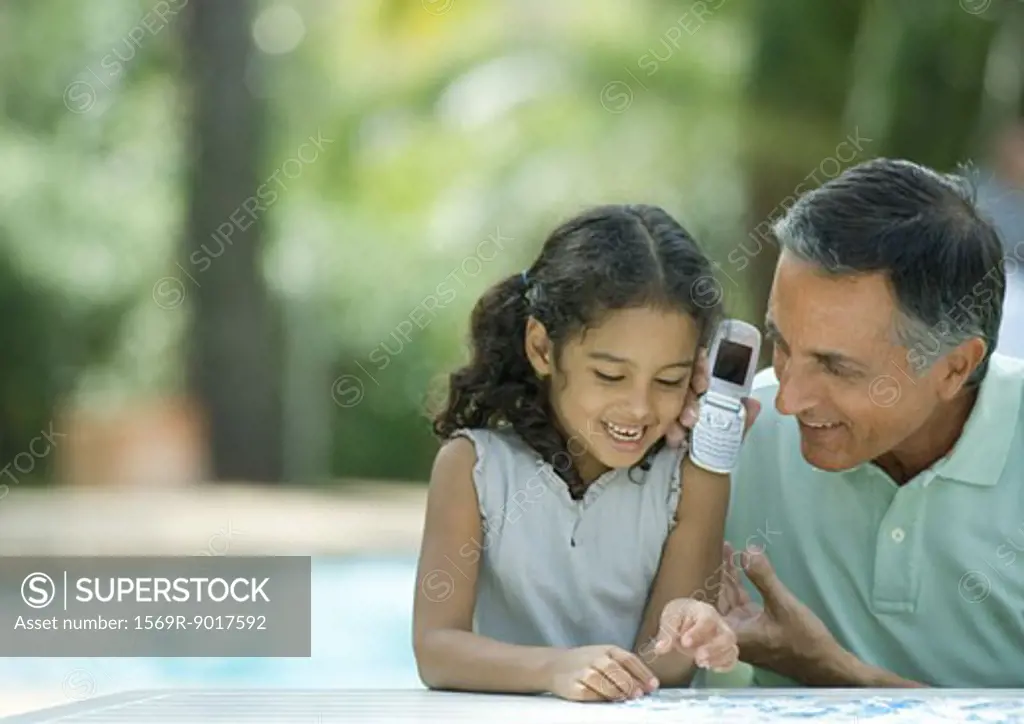 Mature man holding up cell phone to granddaughter's ear