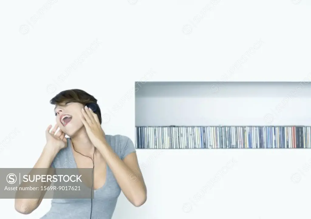 Woman listening to headphones, shelf of cds in background