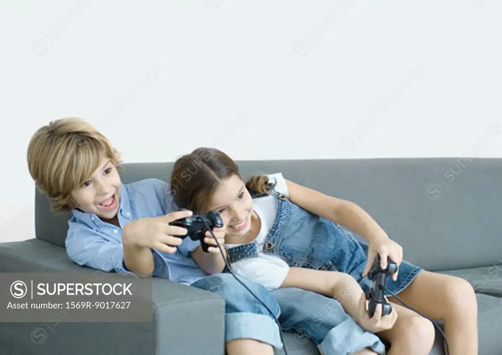 Children sitting on sofa, holding joysticks